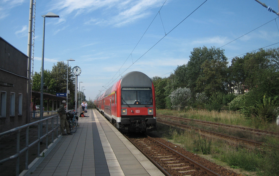 Foto: Ein roter Zug fährt ein, links ist der Bahnsteig mit einigen Personen