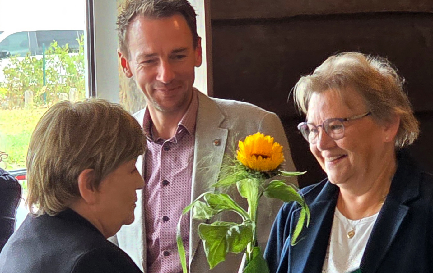 Foto: 3 Personen und ein Sonnenblume wird überreicht