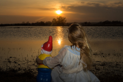 Foto: Mädchen mit Gartenzwerg vor einem Sonneaufgang