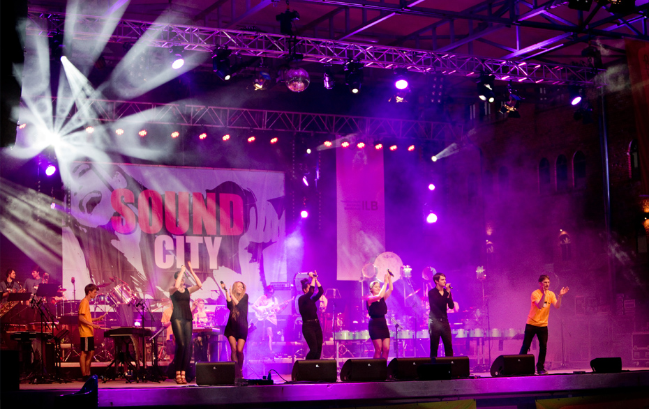 Foto: Sänger und Sängerinnen auf einer farbig beleuchteten Bühne
