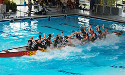 Foto: Drachenboot im Schwimmbecken mit 2 Mannschaften, die sie gegenübersitzen und gegeneinander paddeln