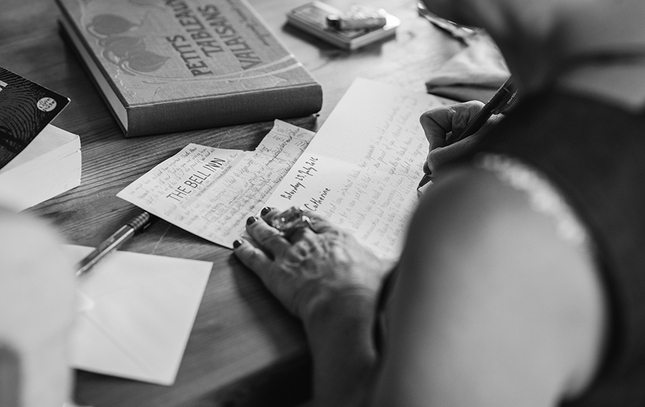 Schwarz-Weiß-Foto: Schreibtisch mit Papieren und einer schreibenden Frauenhand
