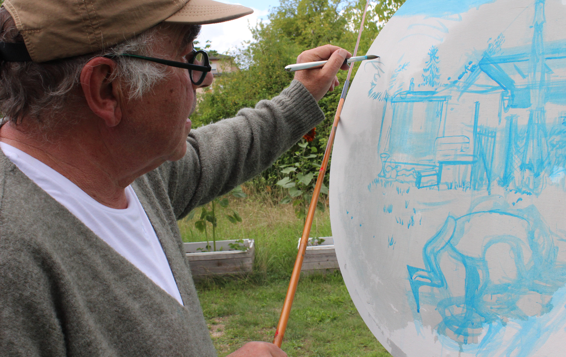 Foto: Künstler malt mit blauer Farbei auf einer runden Fläche