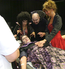 Foto:als Vampir verkleidete Person lässt sich Blut abnehmen und wird von 3 Vampiren beobachtet