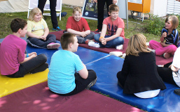Foto: Kinder sitzen auf Sportmatten im Kreis.