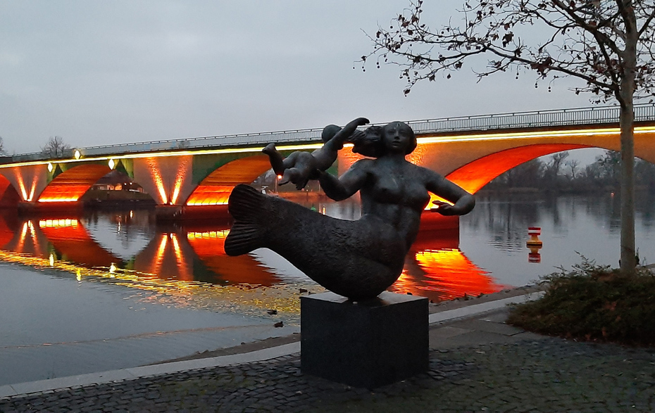 Foto:  Plastik Seejungfrau vor der beleuchteten Brücke