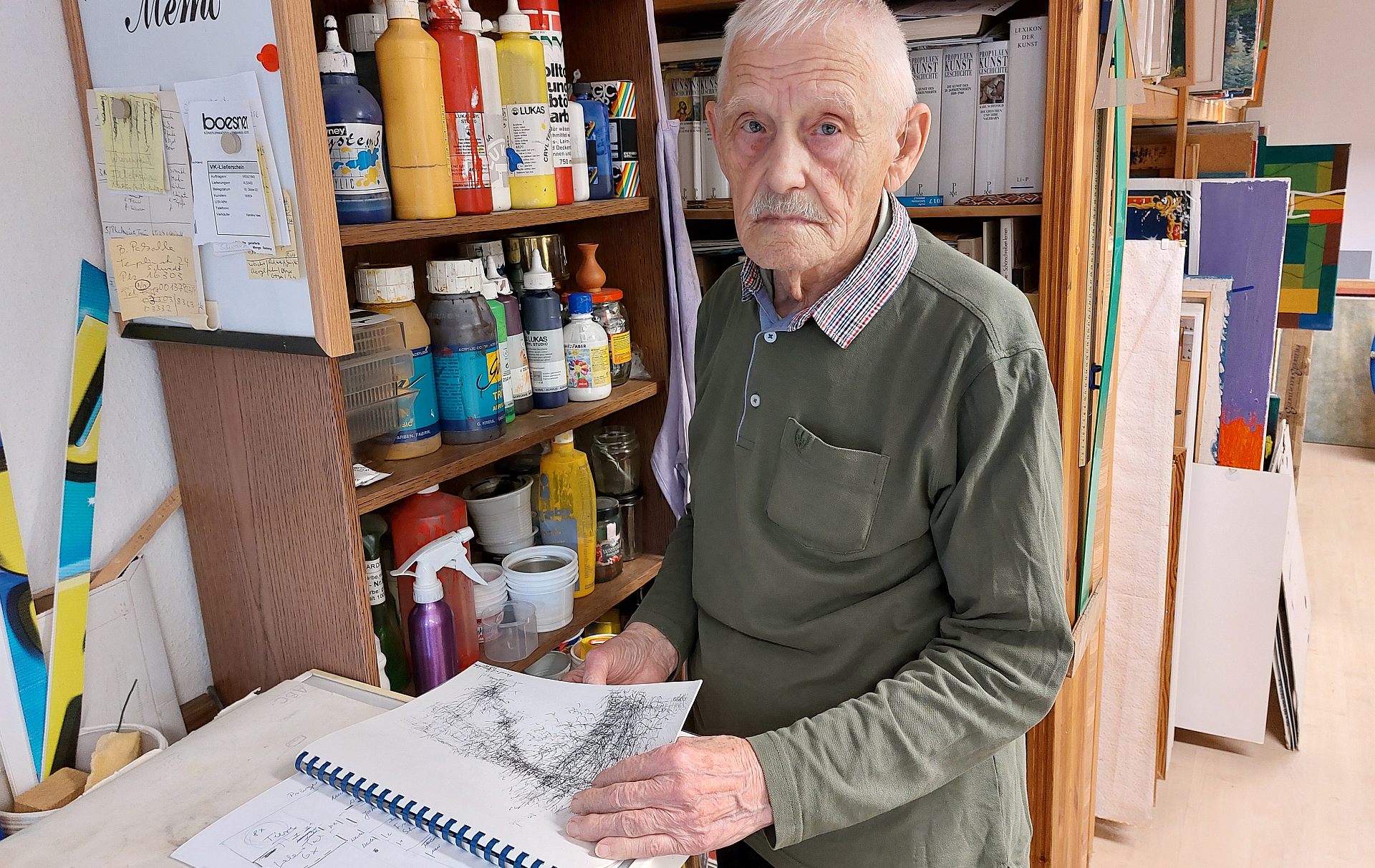 Foto: Künstler vor Regalen mit einem Skizzenblock in der Hand