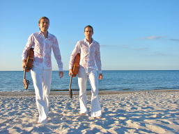 Foto: Zwei Musiker spazieren mit ihren Gitarren am Strand.