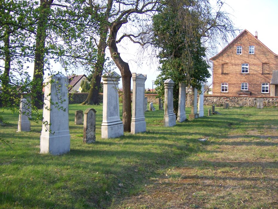 Auf der linken Seite eines unbefestigten Weges stehen hohe und niedrige Grabsteine.