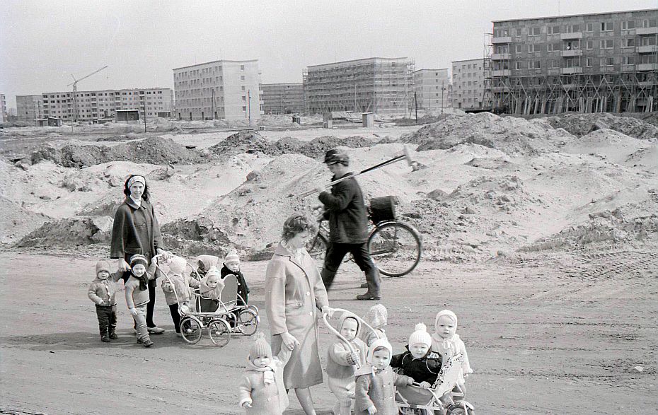 Foto: Krippenkinder laufen an Sandhaufen und Neubaublöcken vorbei.