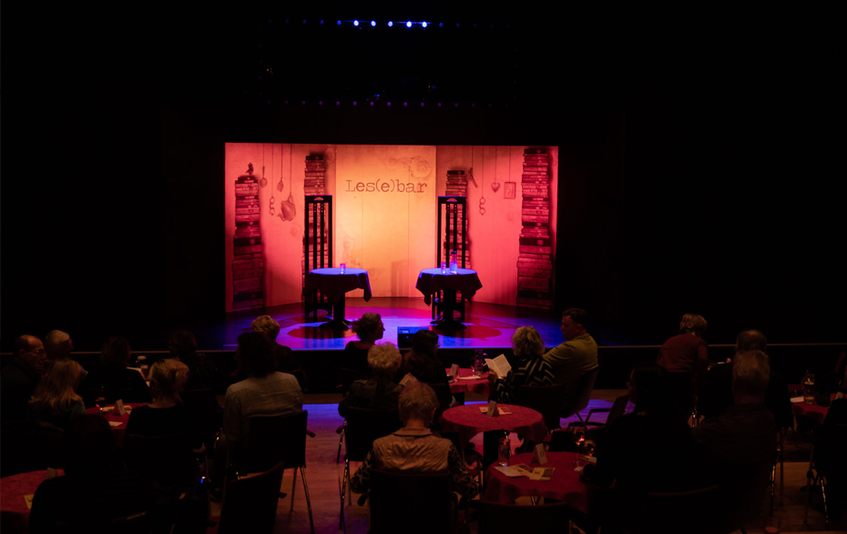 Foto: Blick auf die in Rottönen beleuchtet Bühne über das Publikum hinweg