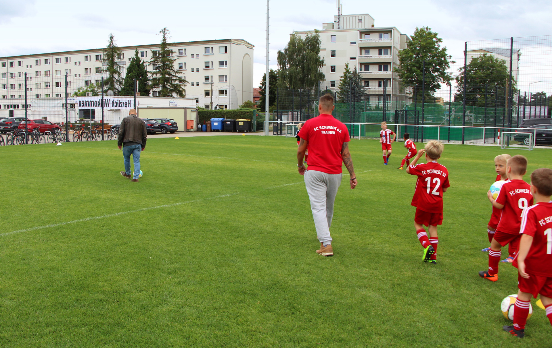 Foto: Fußballmannschaft in roten Trikots läuft auf dem grünen Rasen dem Trainer hinterher