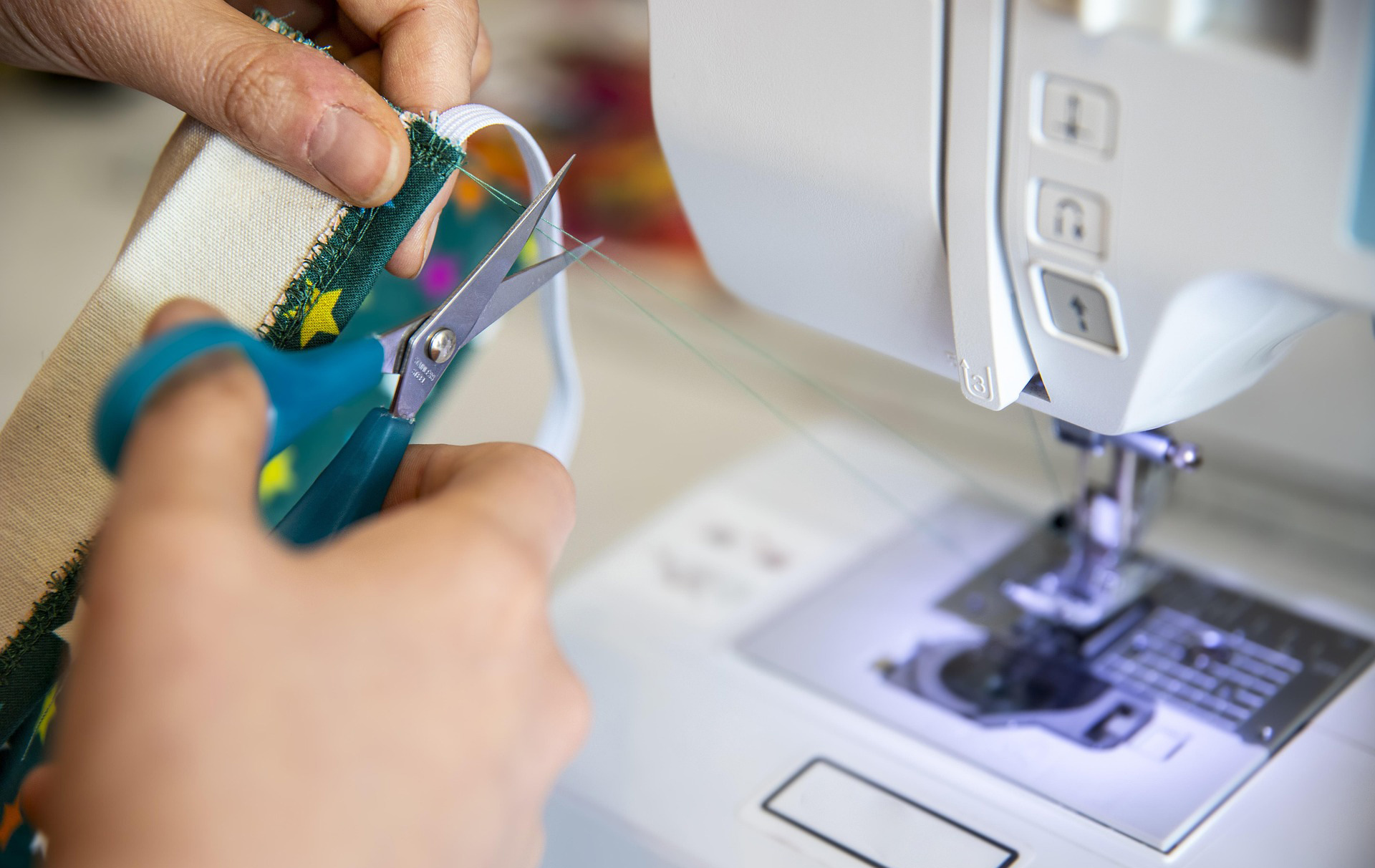 Foto: Hand mit Schere beim Schneiden vor einer Nähmaschine