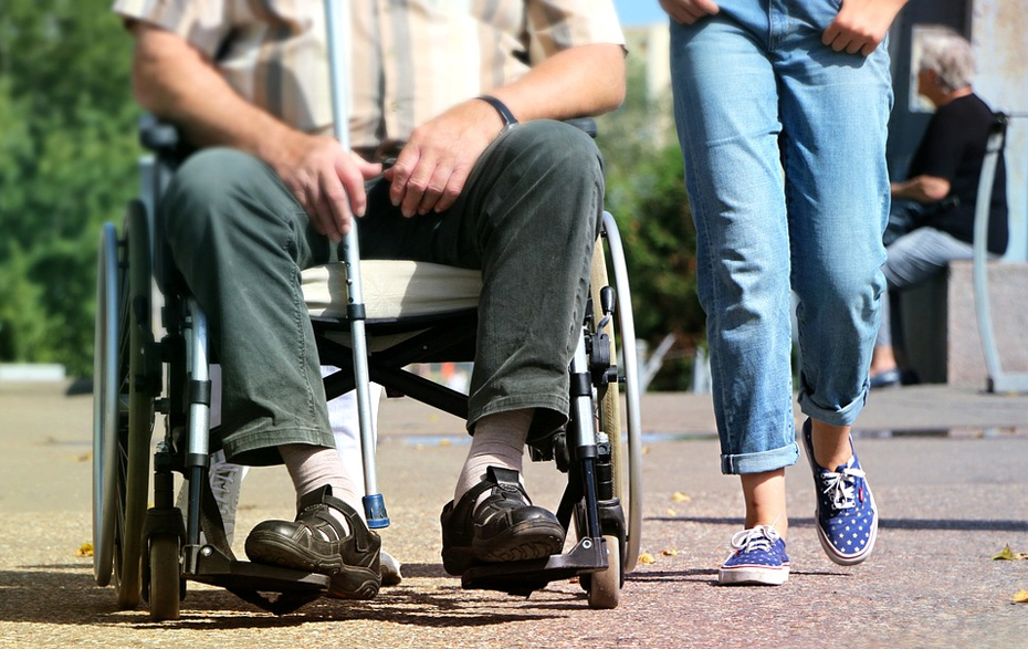 Foto: Senior im Rollstuhl wird von einer jungen Frau begleitet
