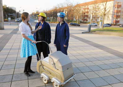 Foto: 3 Personen mit historischem Kinderwagen stehen auf dem Vorplatz der Ubs in Richtung Lindenallee.