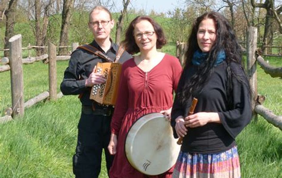 Zwei Frauen und ein Mann halten Instrumenten in der Hand. Sie stehen auf einer Wiese.
