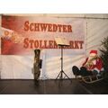 Foto: Bühne mit Banner, Posaune, Notenständer und einer Weihnachtsmannpuppe auf einem Schlitten sitzend