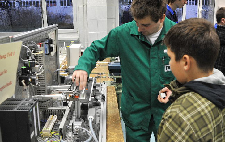 Foto: Ein Auszubildender zeigt einem Schüler seinen Arbeitsplatz.