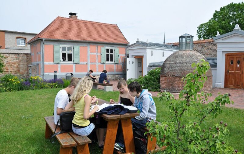 Foto: Schüler*innen sitzen an einem Tisch und lesen. Im Hintergrund ist das Jüdische Museum Schwedt zu sehen.