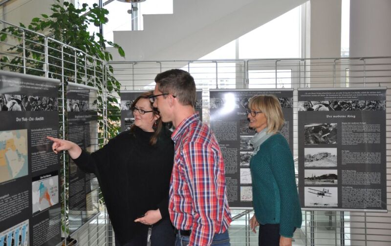 Drei Besucher sehen sich Ausstellungstafeln an. 
