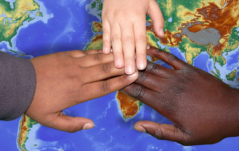 Foto: 3 verschiedenfarbige Hände auf einer Weltkarte