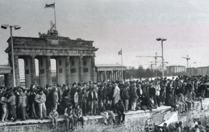 Menschen stehen und sitzen auf der Berliner Mauer