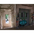 Foto: ein Treppenabsatz und eine Tür, von den Wänden bröckelt die Farbe und sie sind mit Graffiti beschmiert