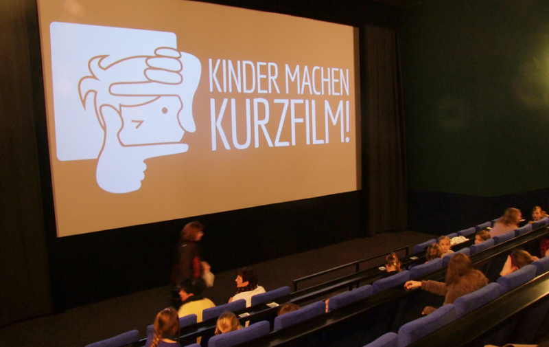 Foto: Kinosaal mit dem „Kinder machen Kurzfilm“-Log auf der Leinwand