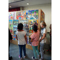 Foto: Drei Mädchen betrachten Bilder an einer Ausstellungswand.
