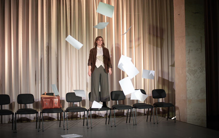 Foto: Schauspielerin steht auf einem Stuhl, Zettel fliegen durch die Luft